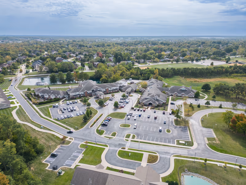 Aerial view of Madonna Manor senior living campus showing multiple connected buildings, parking lots, driveways and surrounding trees and ponds.