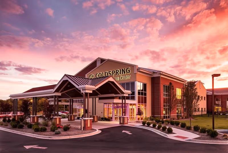 Front entrance of the Coldspring Transitional Care Center building at sunset with a covered porte-cochère and landscaped driveway.