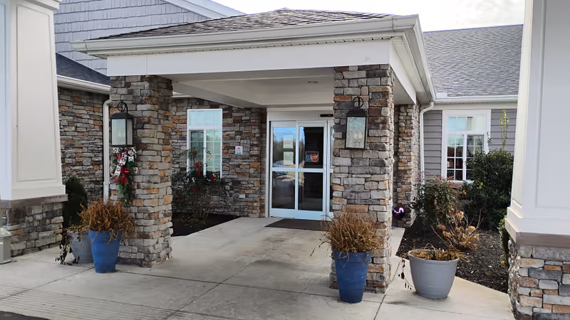 Entrance to a senior living facility with stone columns, glass doors, and potted plants.