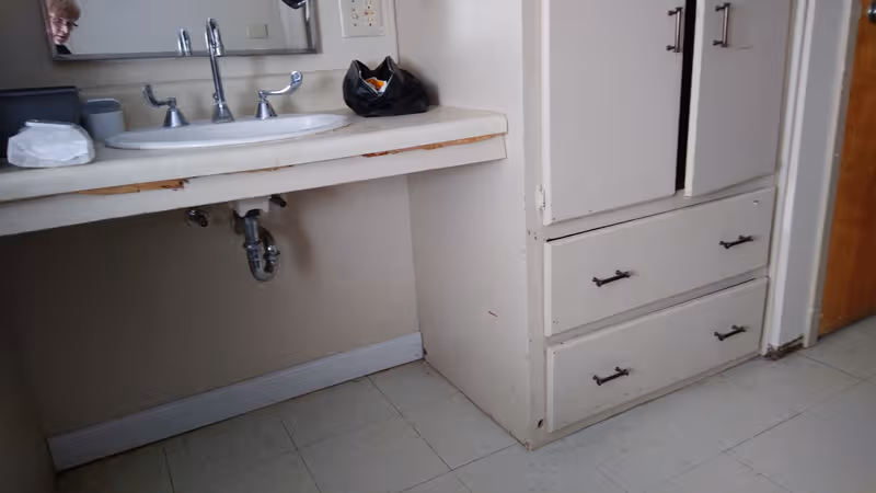 A worn bathroom with sink, faucet, mirror, and a white cabinet with drawers.