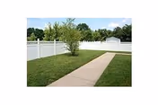 Green lawn with a concrete path and a tree inside a white fenced outdoor area.