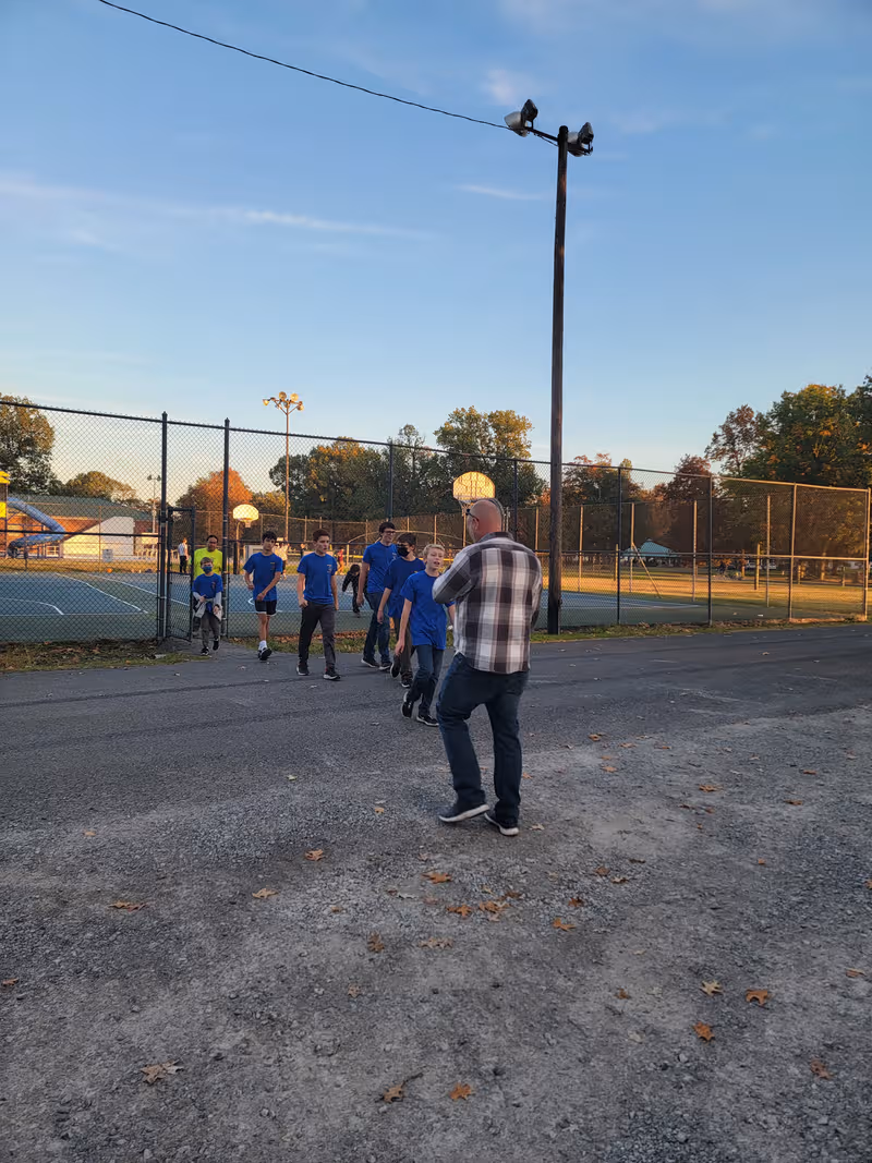 Group of people in blue shirts walk beside a fenced outdoor sports court.