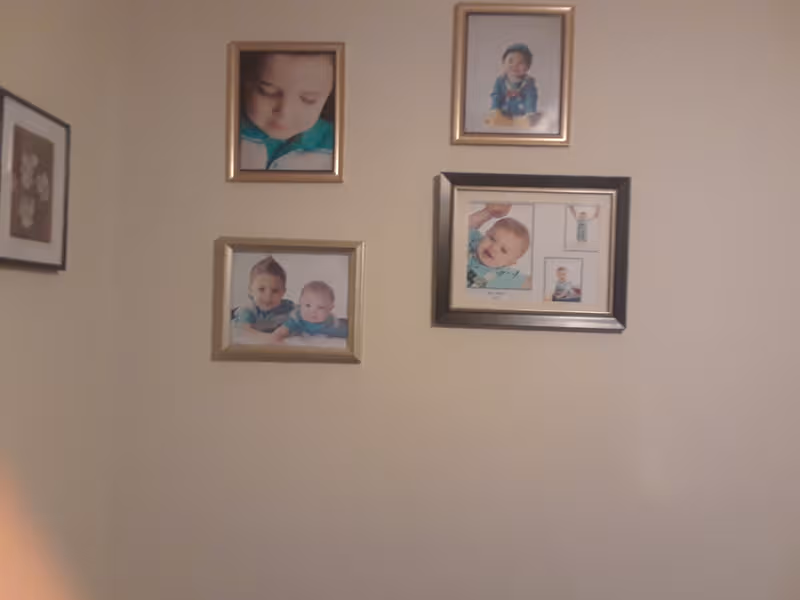 Beige wall adorned with several framed baby photos arranged in a collage.