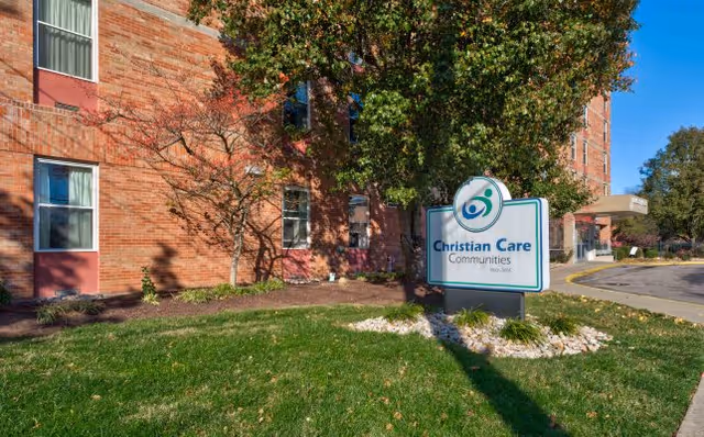 Front exterior of a brick senior living facility with a lawn, trees, and a sign reading "Christian Care Communities" near the entrance.