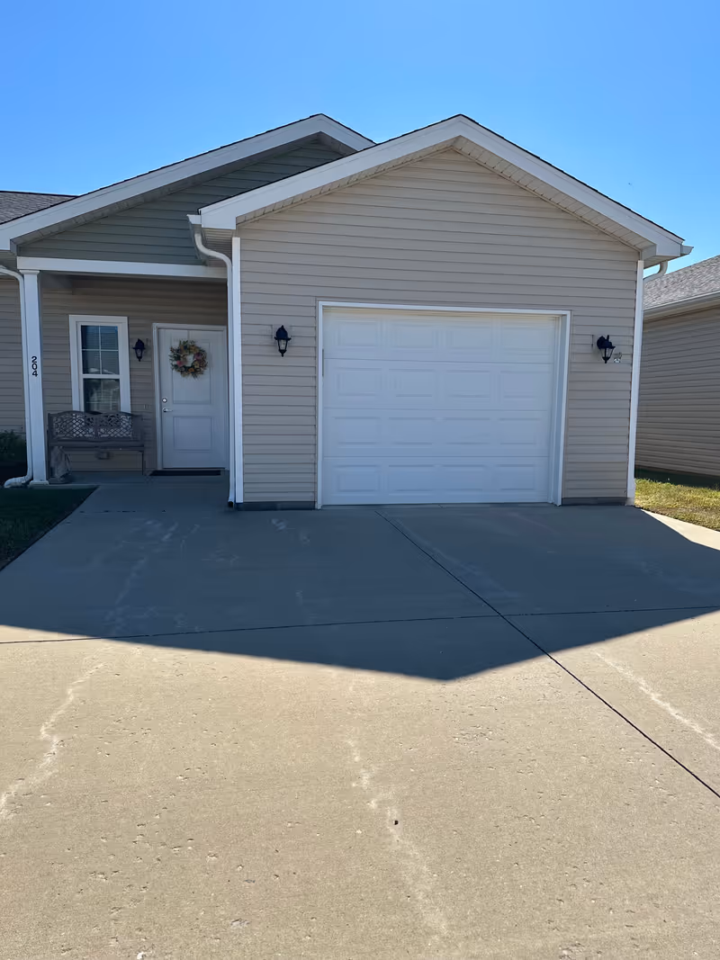 Front exterior of a residential facility with garage, entry door, wreath, and driveway.
