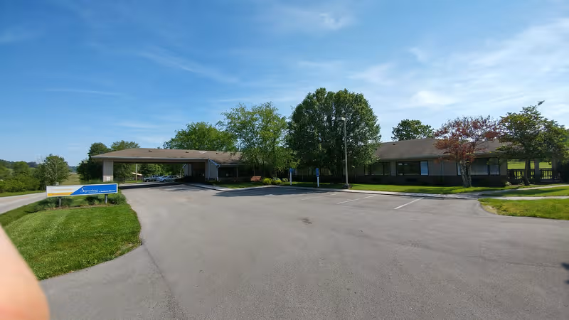 Exterior view of Signature Healthcare at Jackson Manor, showing driveway, entrance, and surrounding trees.