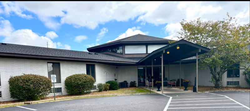 Exterior view of a senior living facility with a covered entrance and parking area.