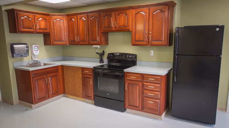 Small kitchen with cherry wood cabinets, a black stove and refrigerator, a sink, and pale green walls.