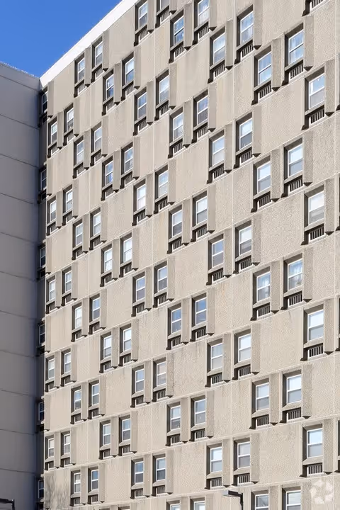 Exterior view of a multi-story building with numerous windows arranged in a grid pattern under a clear blue sky.