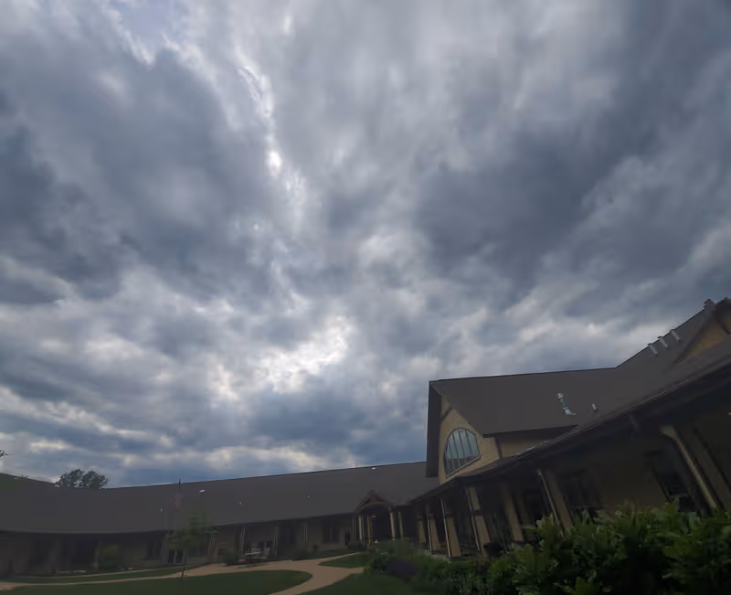 Overcast sky looms over the senior living facility exterior with a curved entrance and path.