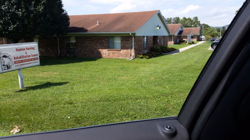 Brick nursing center building with green lawn and sign in front.