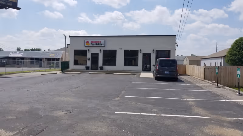 A single-story commercial building with a parking lot, a minivan, and a sign reading Unlimited Possibilities.