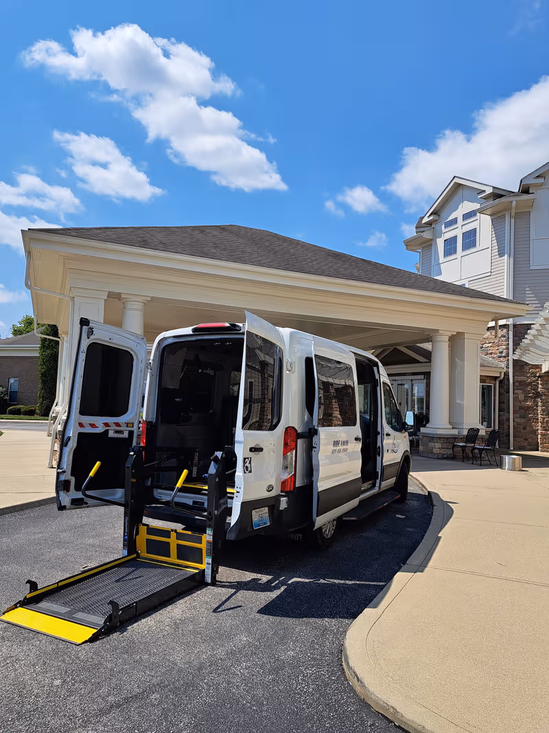 Accessible van with deployed ramp parked at the front entrance of a senior living facility.