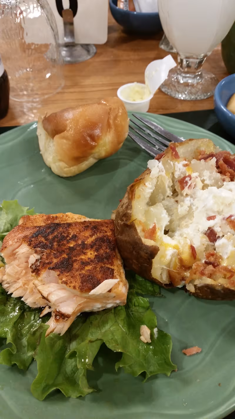 Plate of seared salmon with greens, a roll, and a loaf slice on a dining table.