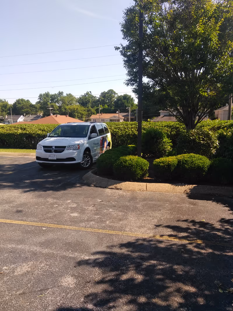 White van parked in a lot by hedges and trees at Princeton Health & Rehab Center