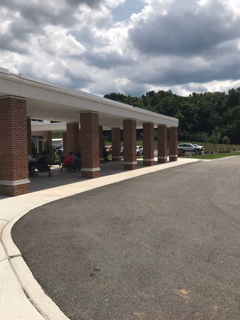 Covered entrance with brick columns at The Seasons at Alexandria; cars parked nearby.