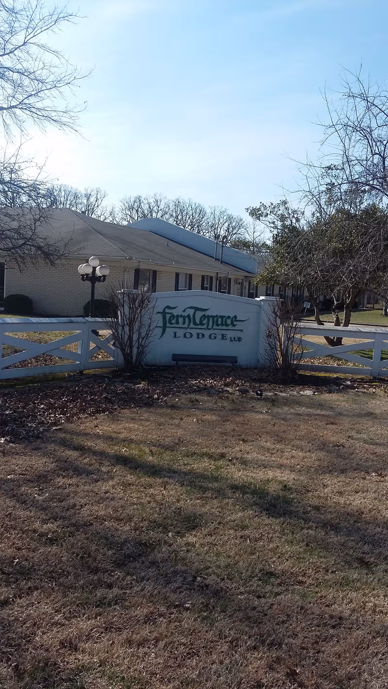 Exterior view of Fern Terrace Lodge sign, white fence, and single-story building.