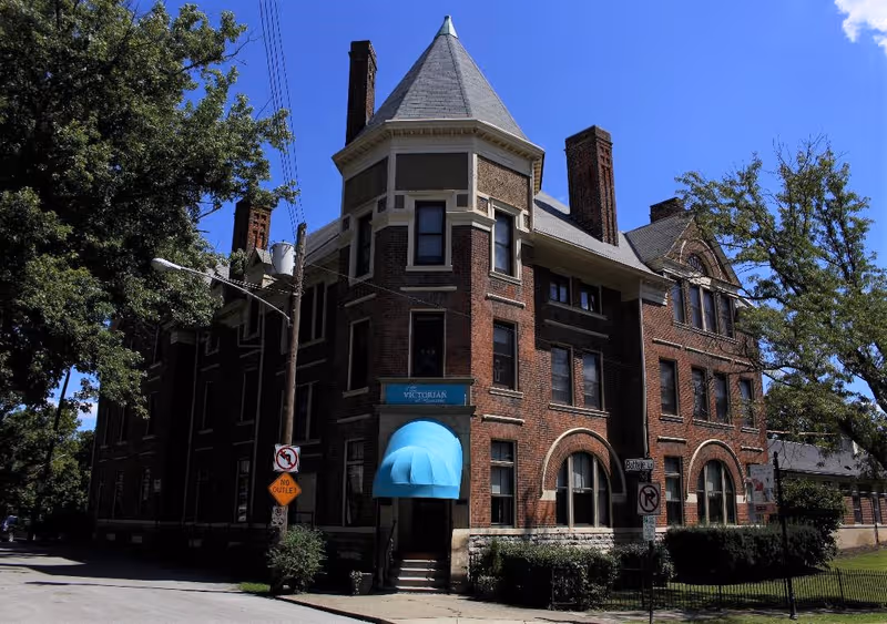 Brick senior living building with a blue entrance awning and turret tower.