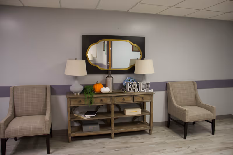 Two beige armchairs flank a wooden console with lamps, pumpkins, and a decorative mirror.