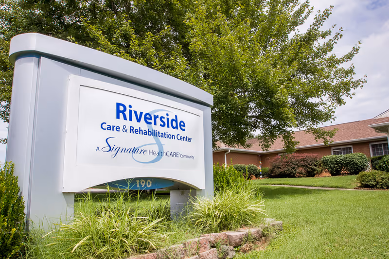 Front exterior of Riverside Care & Rehabilitation Center with a large sign and landscaping