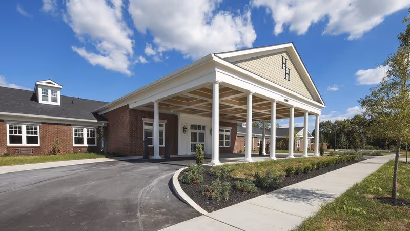 Exterior view of Hallmark House senior living facility with a columned entrance and brick facade.