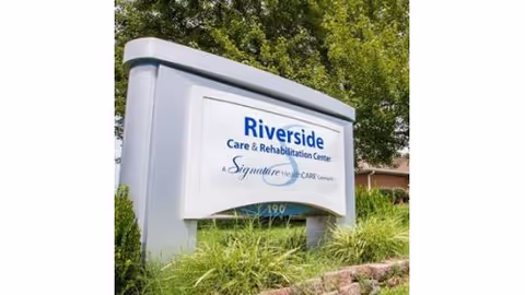 Outdoor sign for Riverside Care & Rehabilitation Center amid greenery.