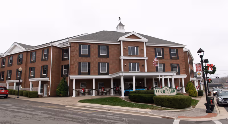 Brick senior living facility named The Courtyard with a covered entrance and American flag.
