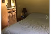 Bedroom in a senior facility with bed, nightstand, lamp, and doorway to dining area