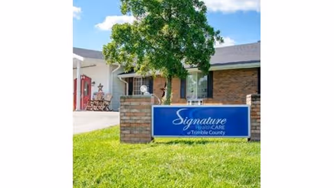 Brick facility front with a blue 'Signature HealthCARE of Trimble County' sign on a grassy lawn and a tree in front.