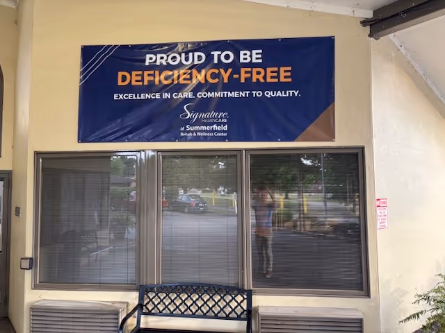 Front entrance of Signature HealthCARE at Summerfield with a deficiency-free banner above glass doors.