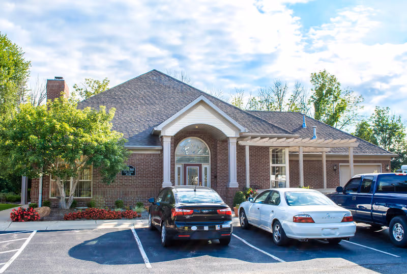 Front view of a brick senior living facility with arched entrance and parked cars.