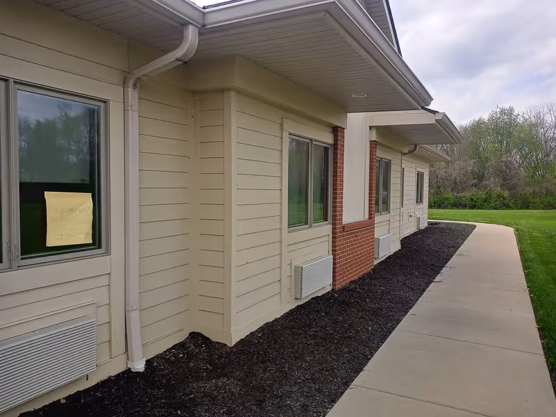 Exterior view of a beige senior living building with a walkway and lawn.