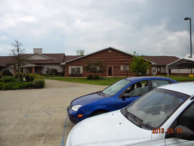 Exterior view of Twin Oaks Assisted Living with a parking lot and blue and white cars.