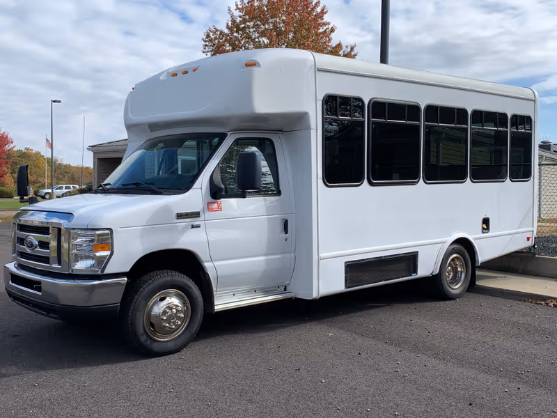 White shuttle bus parked in a lot beside River's Bend Retirement Community