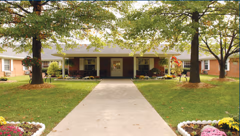 Front view of a senior living facility with a central walkway and mature trees.