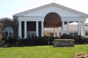 Front entrance of Windsor Care Center with a white columned portico and a stone sign on a grassy lawn.