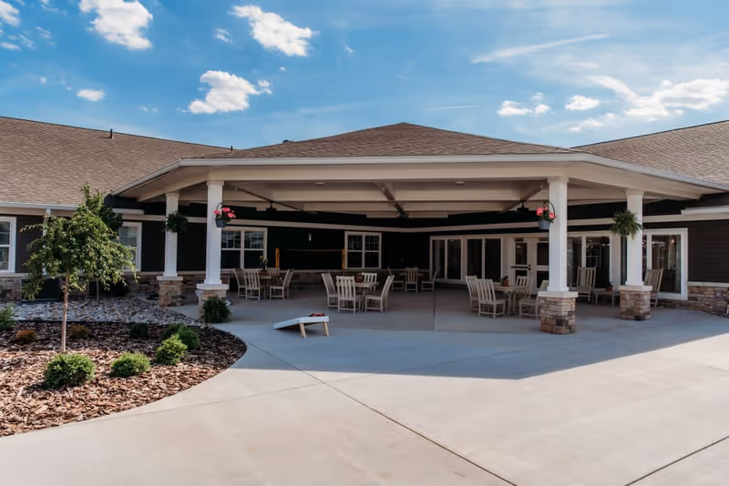 Covered outdoor patio with tables and chairs in front of a single-story senior living building.