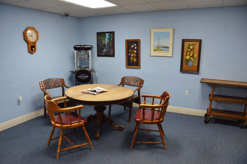 Light blue walls surround a round wooden table with four chairs in a small lounge.