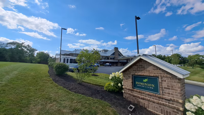 Exterior view of Dominion Senior Living facility with brick sign, landscaped lawn, and entrance.