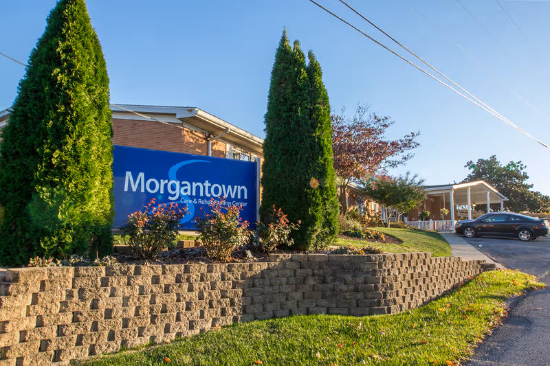 Exterior view of Morgantown Care & Rehabilitation Center with blue sign and landscaping.