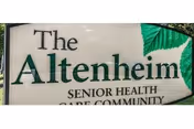 Close-up view of a sign for The Altenheim Senior Health Care Community with a green leaf graphic on the right side.