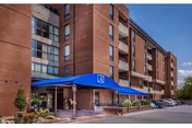 Brick senior living building with blue awning entrance and parked cars along driveway.
