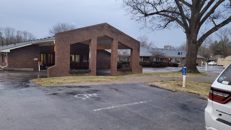 Exterior view of Signature Healthcare at Heritage Hall, brick entrance, parking, and a tree.