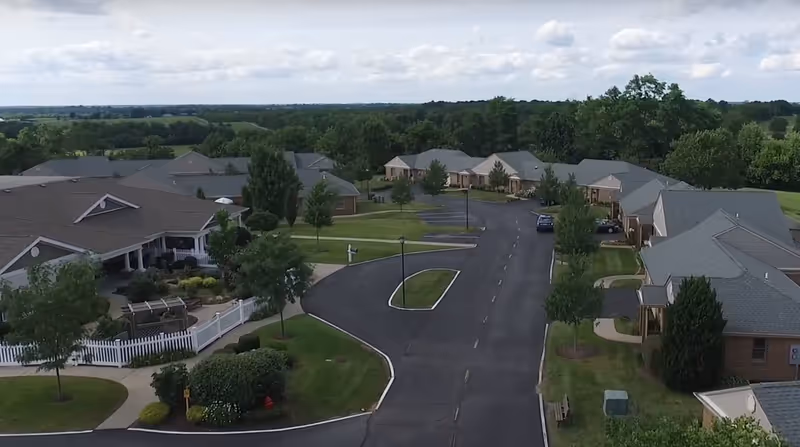 Aerial view of the Wesley Village Senior Living campus with single-story residences, a curved driveway, lawns and trees.