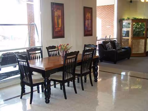 A dining area in a senior living lobby with a wooden table, chairs, and a sofa.