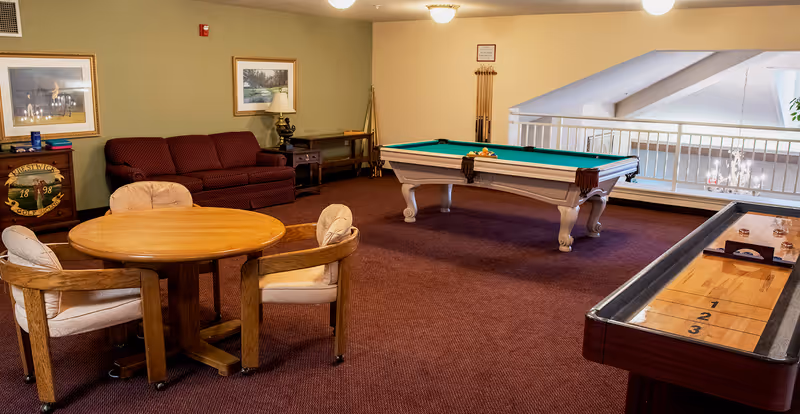 Recreation room with a pool table, shuffleboard, round table and chairs, and a seating area with a couch.