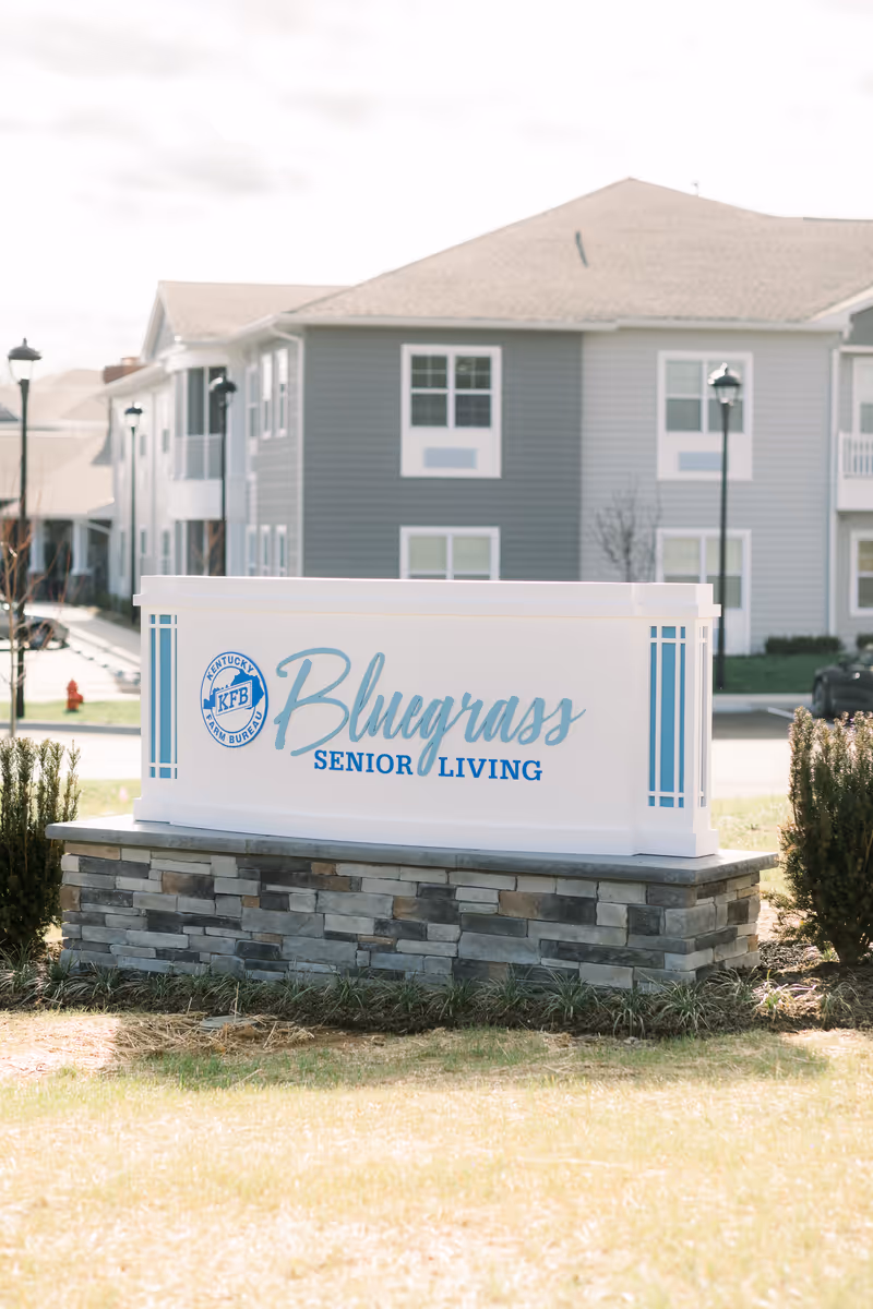 Sign for Bluegrass Senior Living sits on a stone pedestal in front of a gray building.