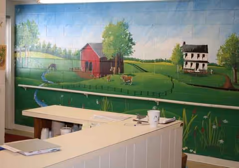 Reception desk in a mural-painted interior lobby with pastoral countryside wall art.
