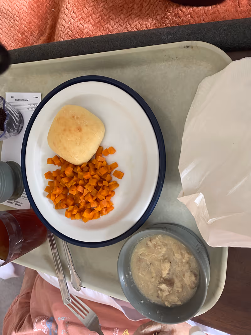 Meal tray with diced carrots, a bread roll, and a bowl of soup.