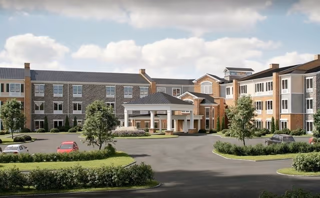 Front exterior of a multi-story senior living facility with a covered porte-cochère entrance, landscaped driveway, and parked cars.